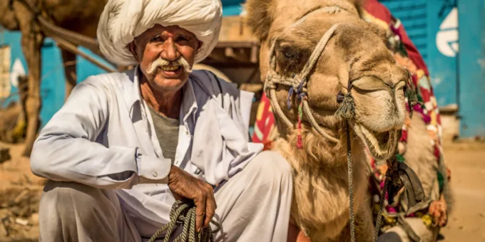 A working camel looks content as it sits next to its smiling owner in India.