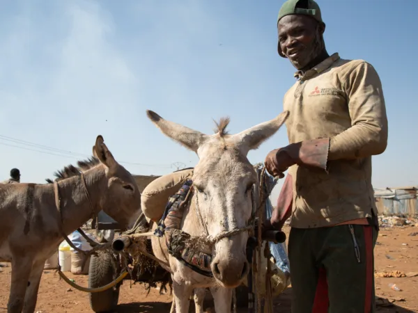 Belima the donkey stands staring at the camera. To his right is his owner. In the background is the rubbish dump they work at together